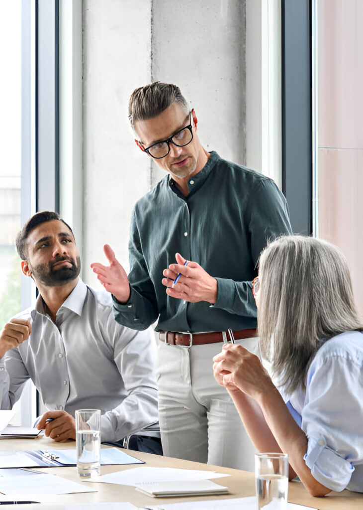 Three professionals engaged in a discussion around a meeting table with documents.